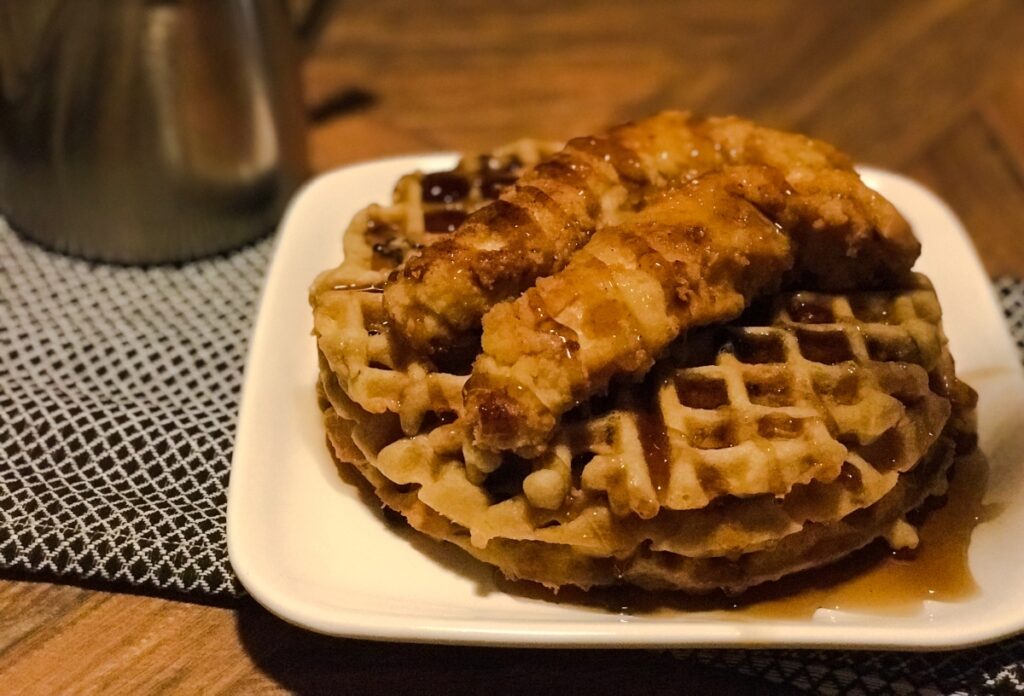 chicken and waffles served on a plate with drizzled syrup over dish 