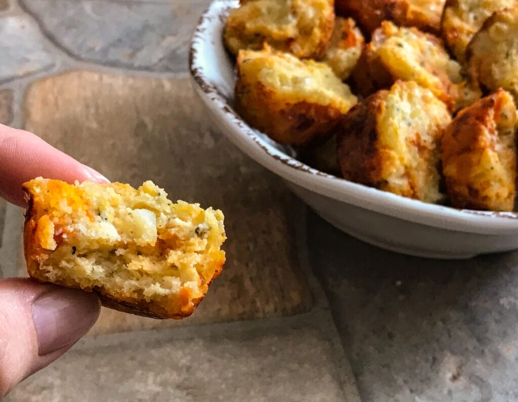 a bitten into view of the pizza muffin next to the rest of the pizza muffins in a bowl