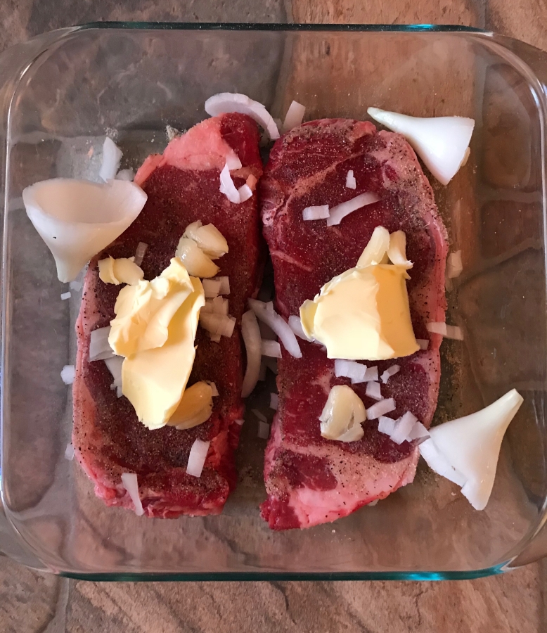 uncooked steak in a glass dish with seasoning preppering to go into oven