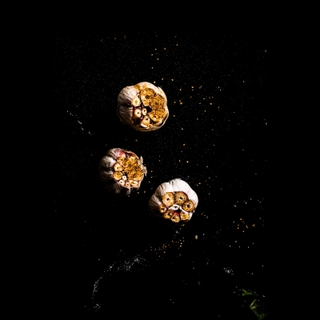Three heads of roasted garlic on a dark surface