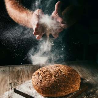 Hands dusting flour over a freshly baked loaf