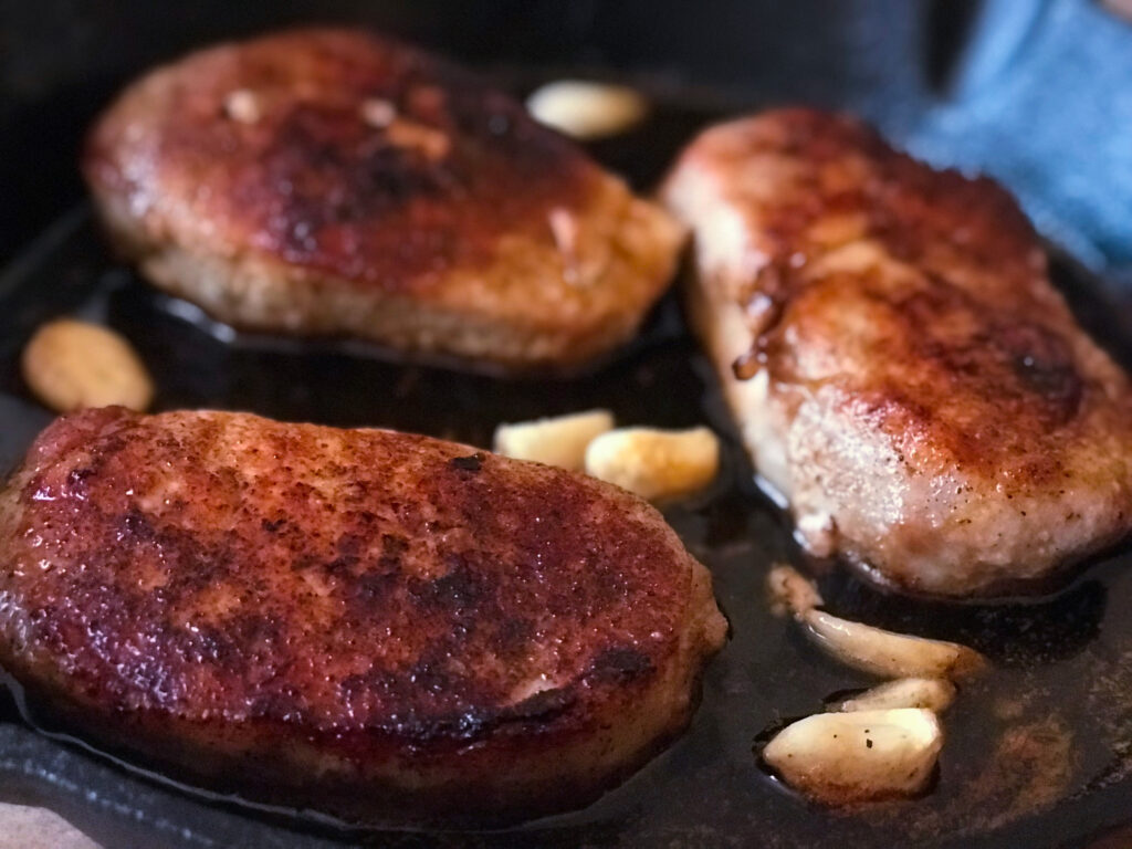 close up side view of pork chops in a skillet pan 