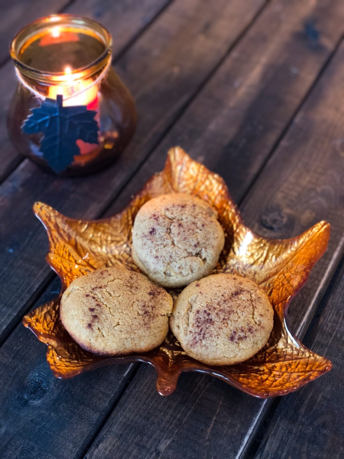 three pumpkin cookies on a fall designed leaf plate next to a pumpkin scented candle