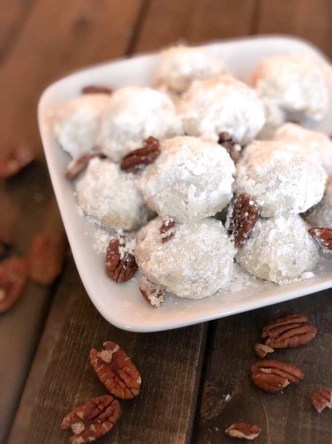 photo of snowball cookies on a platter and pecan scattered on the wooden table