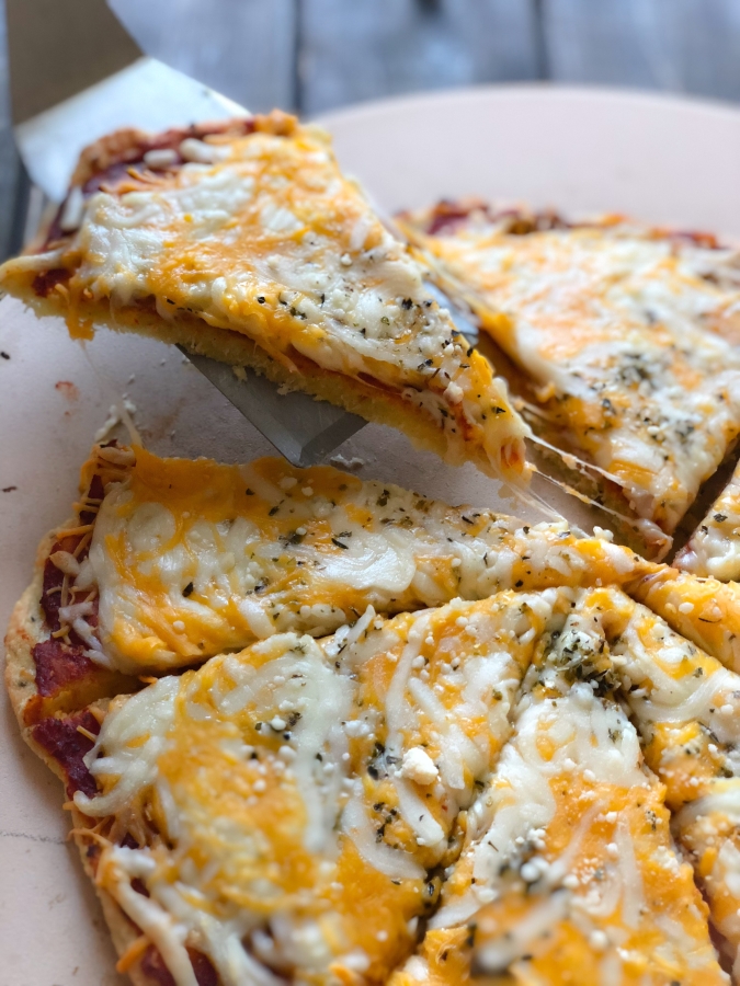 cheesy keto pizza with a slice being lifted off the pizza stone