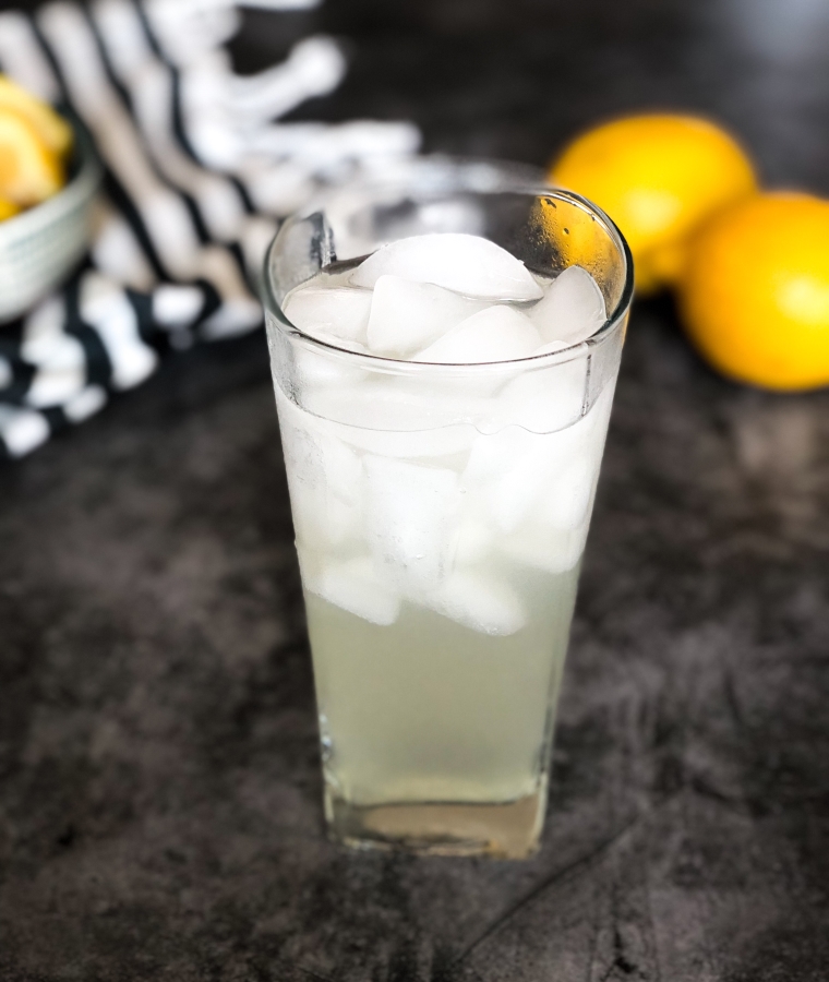 one tall glass of keto lemonade with lemons in the background 