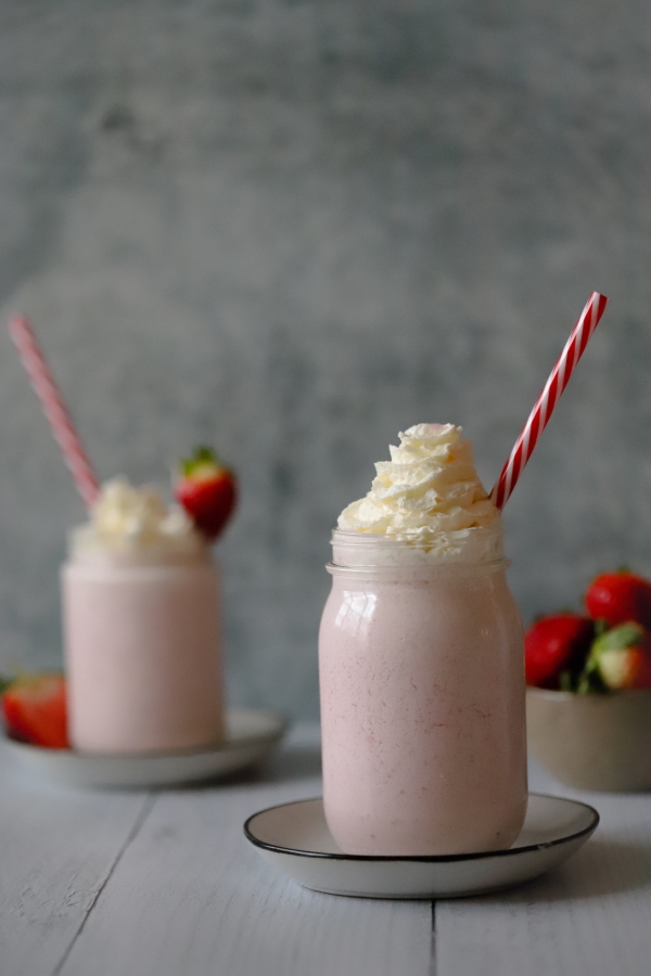 two strawberry cheesecakes shakes with a bowl of strawberries in the background