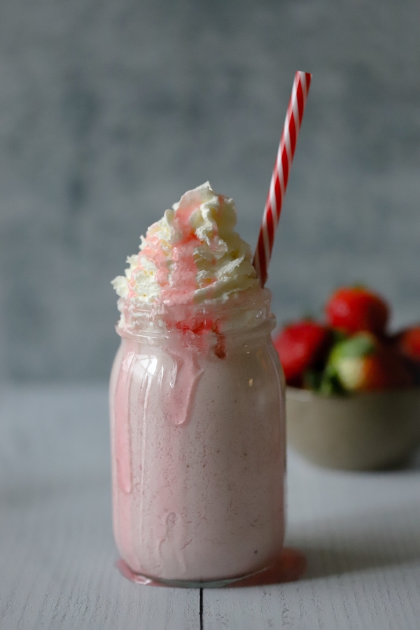 strawberry cheesecake shake in the center with a bowl of strawberries in the background
