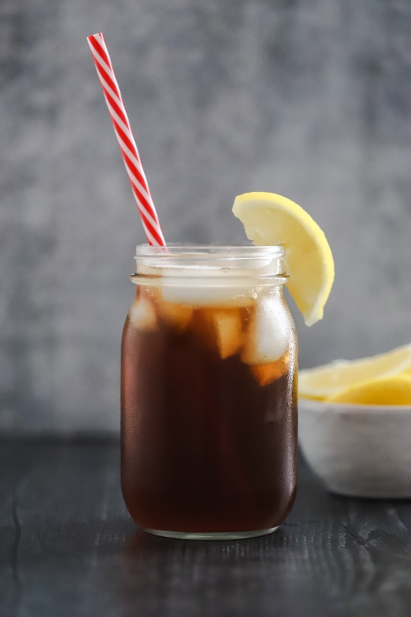one glass of sweet tea in a mason jar with a bowl of lemons in the background