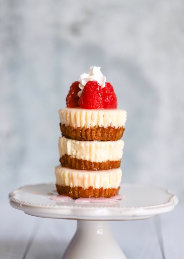 three mini cheesecake stacked up on each other with raspberries and whipped cream on top