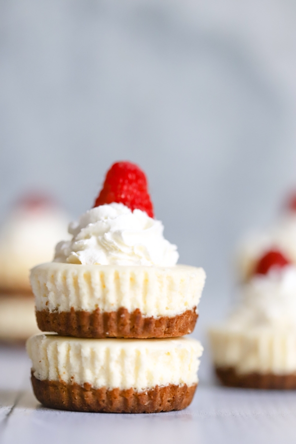 zwei Mini-Käsekuchen übereinander mit etwas Sahne und Himbeere. Mehr Mini-Käsekuchen im Hintergrund