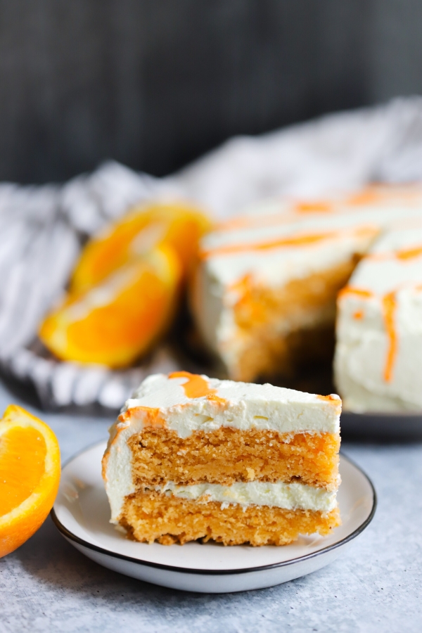 a single slice of orange creamsicle cake with the rest of the cake in the background