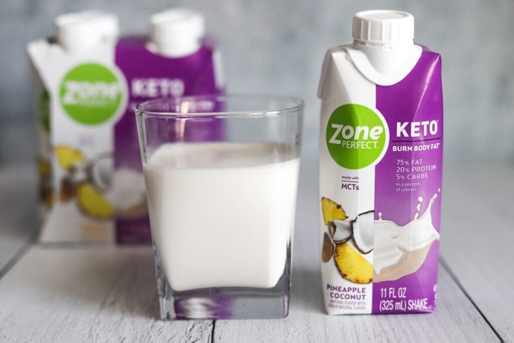 photo of a glass of ZonePerfect pineapple coconut keto shake with the package next to it and box behind the glass