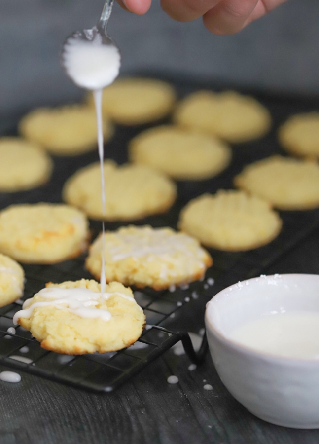 spoonful of glaze hovering over freshly baked lemon cookies being glazed