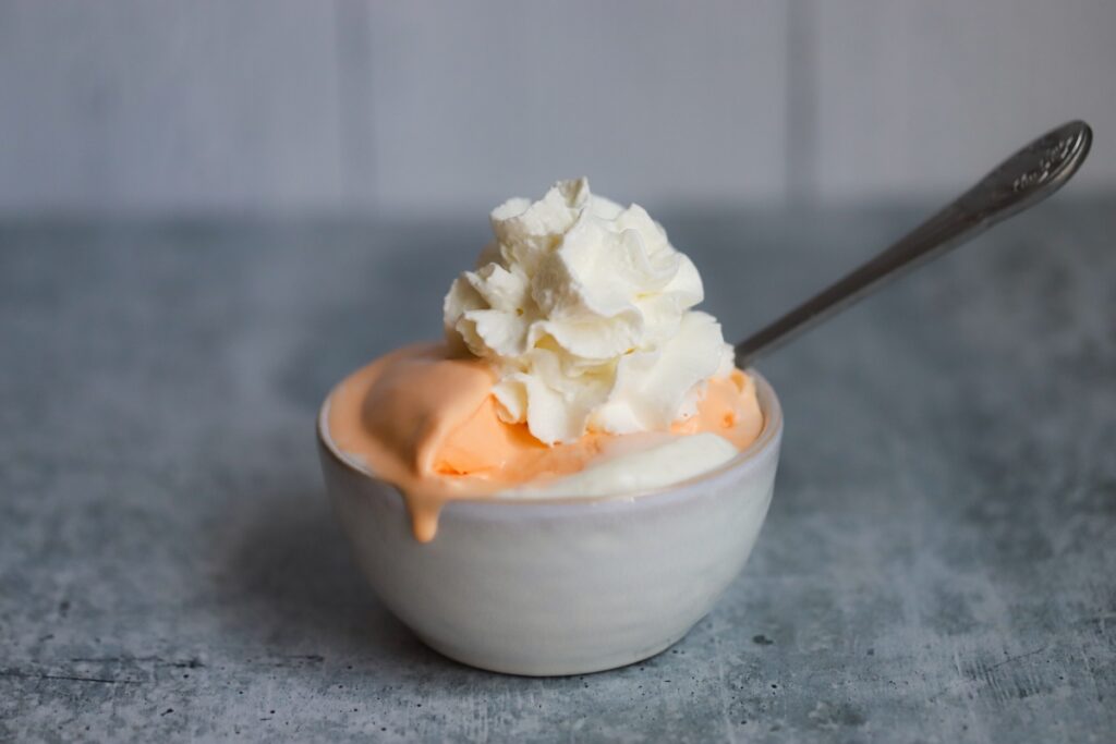 a bowl of orange creamsicle ice cream in the center with whipped cream on top