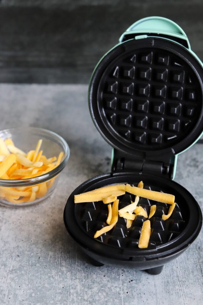 mini waffle maker with some shredded cheese on it and a bowl of shredded cheese on the side