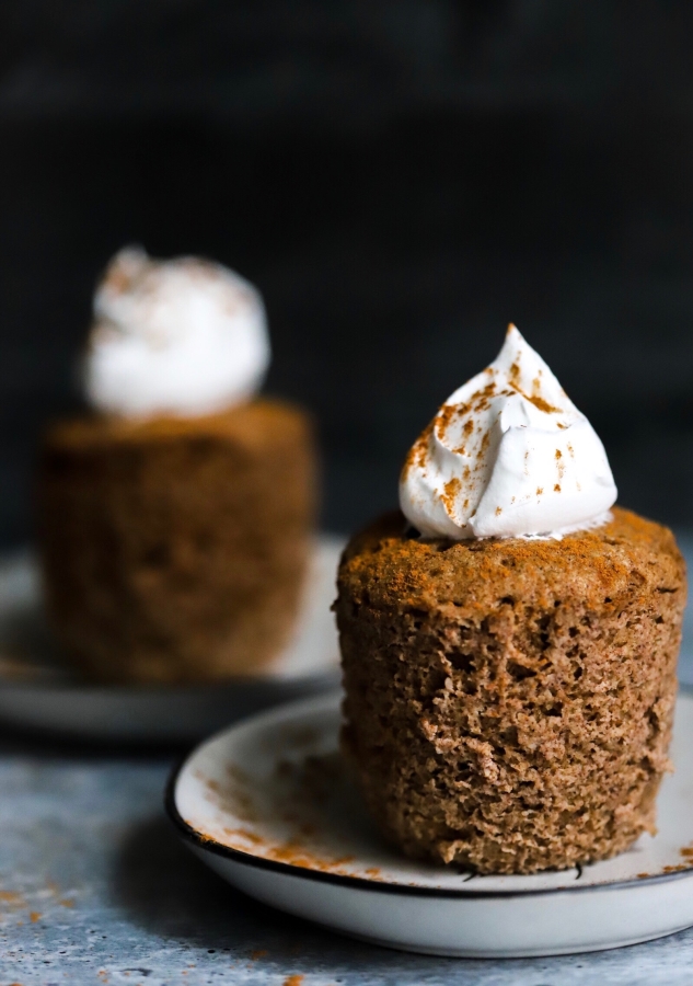 two keto pumpkin mug cakes outside the mug and on a plate. One mu cake in the front with one in the back and blurred a little.