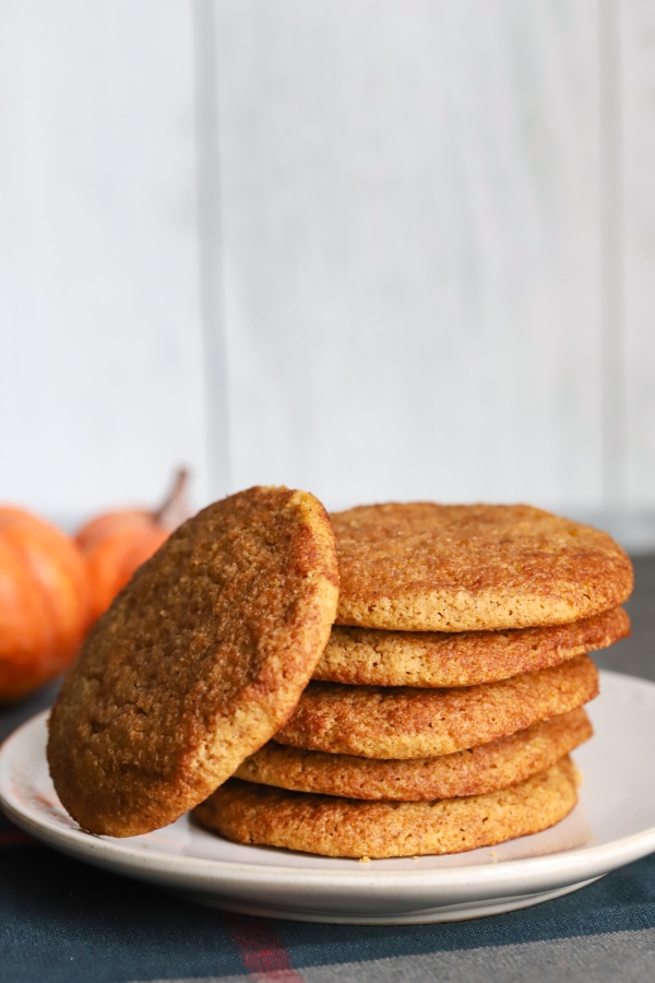 a stack of pumpkin snickerdoodle cookies with one slanted leaning next to the stack of cookies on a plate