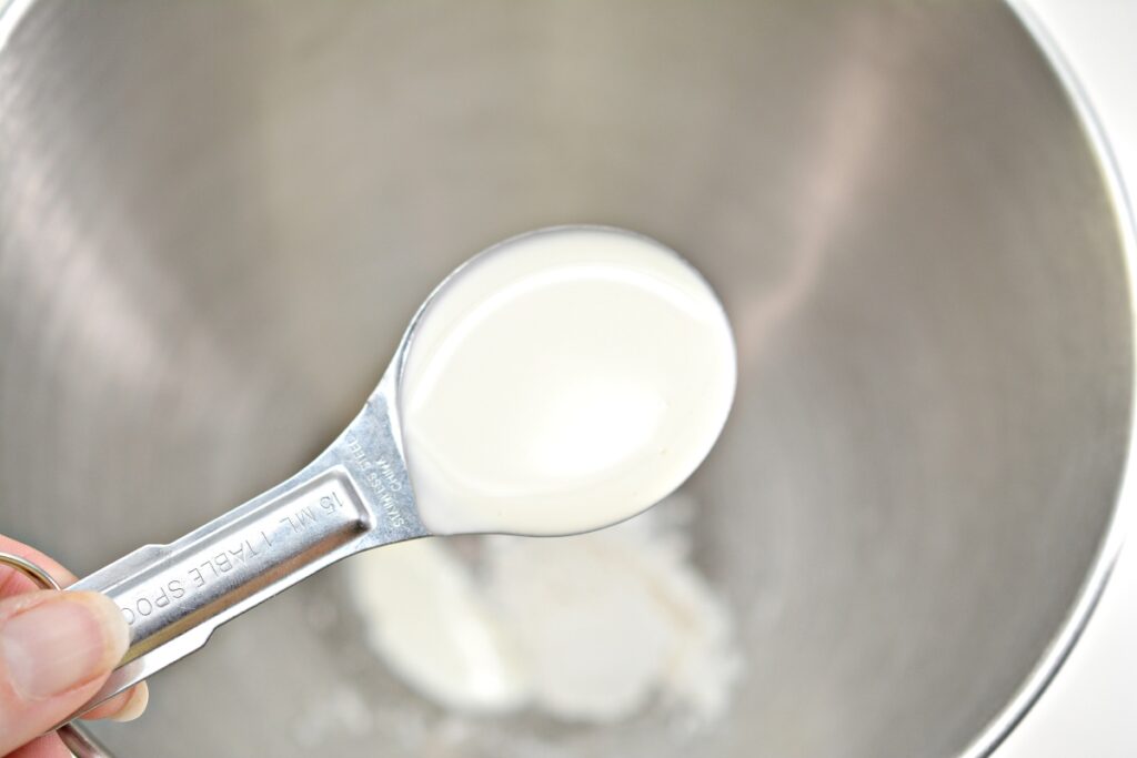 heavy whipping cream in a measuring spoon over a mixing bowl