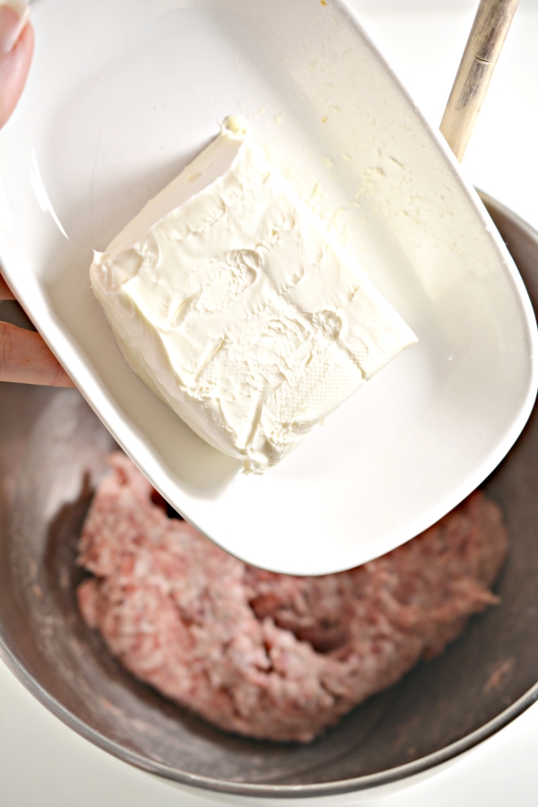 cream cheese being tossed into mixing bowl with sausage