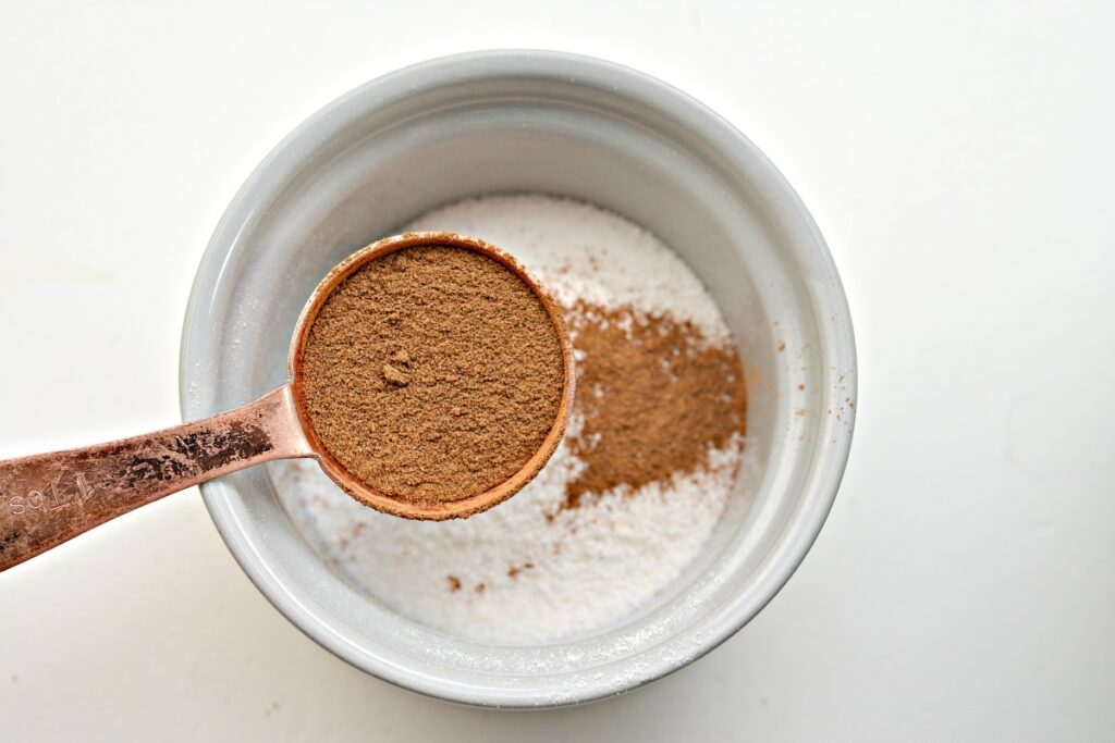 measuring spoon with cinnamon over a small bowl