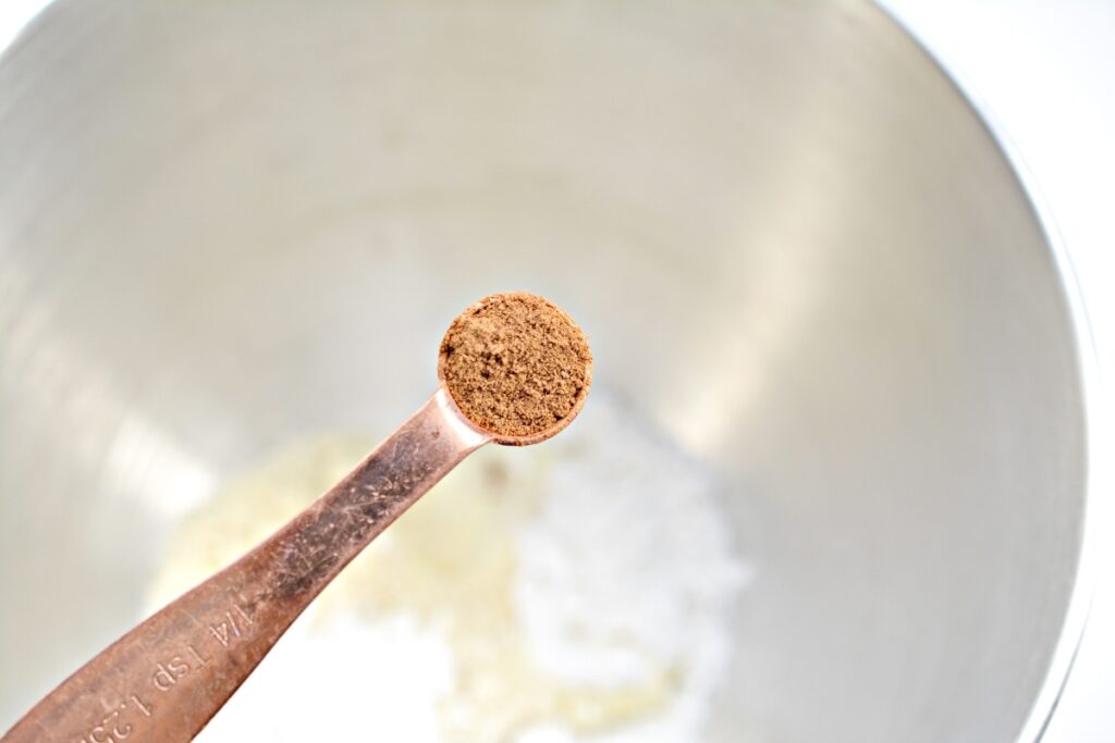 measuring spoon with apple pie spice over a mixing bowl