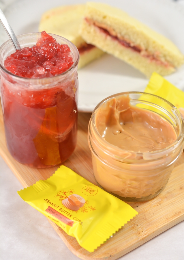 peanut butter and jelly in jars with a cut in half peanut butter and jelly sandwich behind the jars 