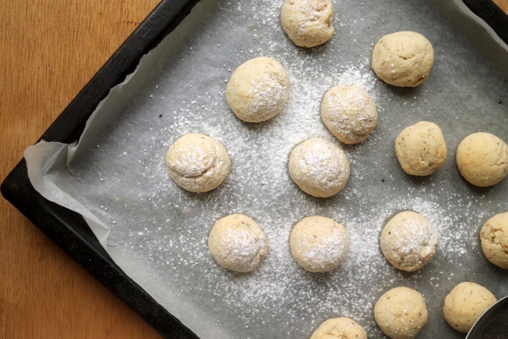 adding powdered sweetener to snowball cookies on a baking sheet