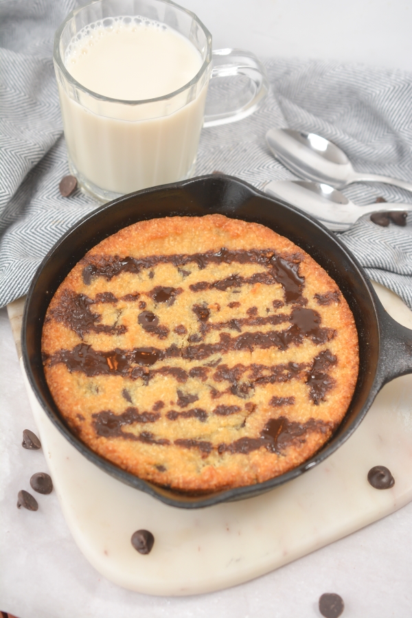keto chocolate chip skillet cookie with a tall glass of milk and two spoons in the background
